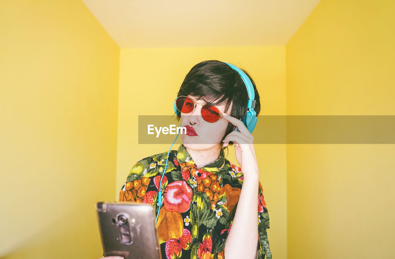 Woman wearing sunglasses using phone against colored background