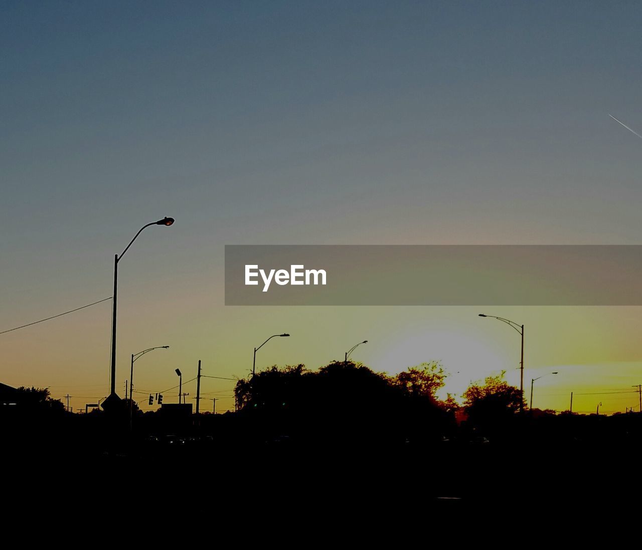 SILHOUETTE STREET LIGHTS AGAINST SUNSET SKY