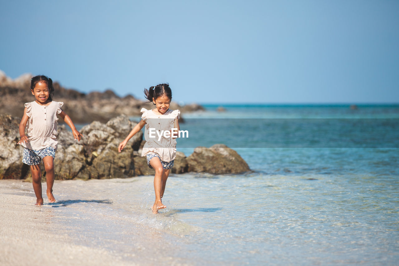 Full length of girls running at beach against clear sky