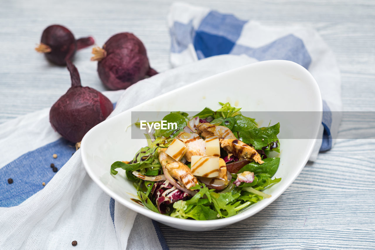 Deep bowl of arugula salad with cheese and chicken fillet slices. dressed with balsamic sauce.