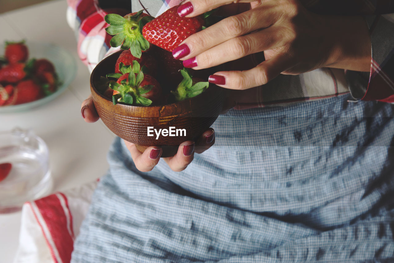 Midsection of woman holding strawberries in bowl at home