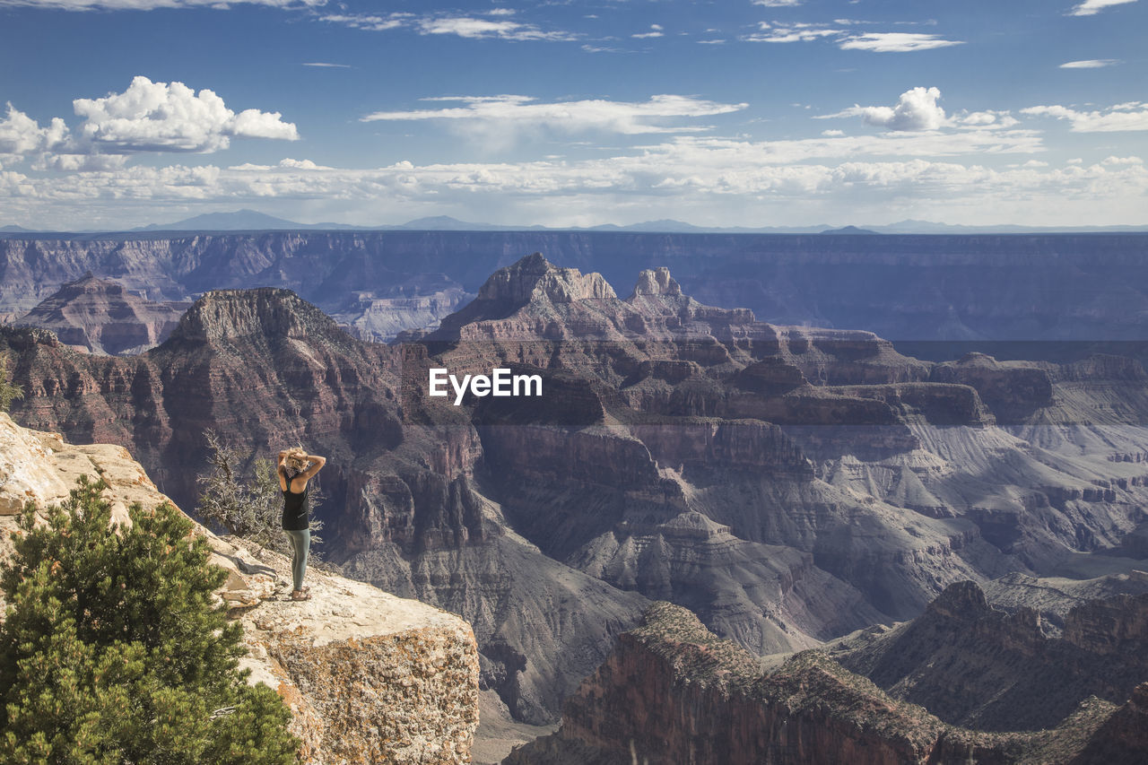 REAR VIEW OF PEOPLE LOOKING AT MOUNTAINS AGAINST SKY