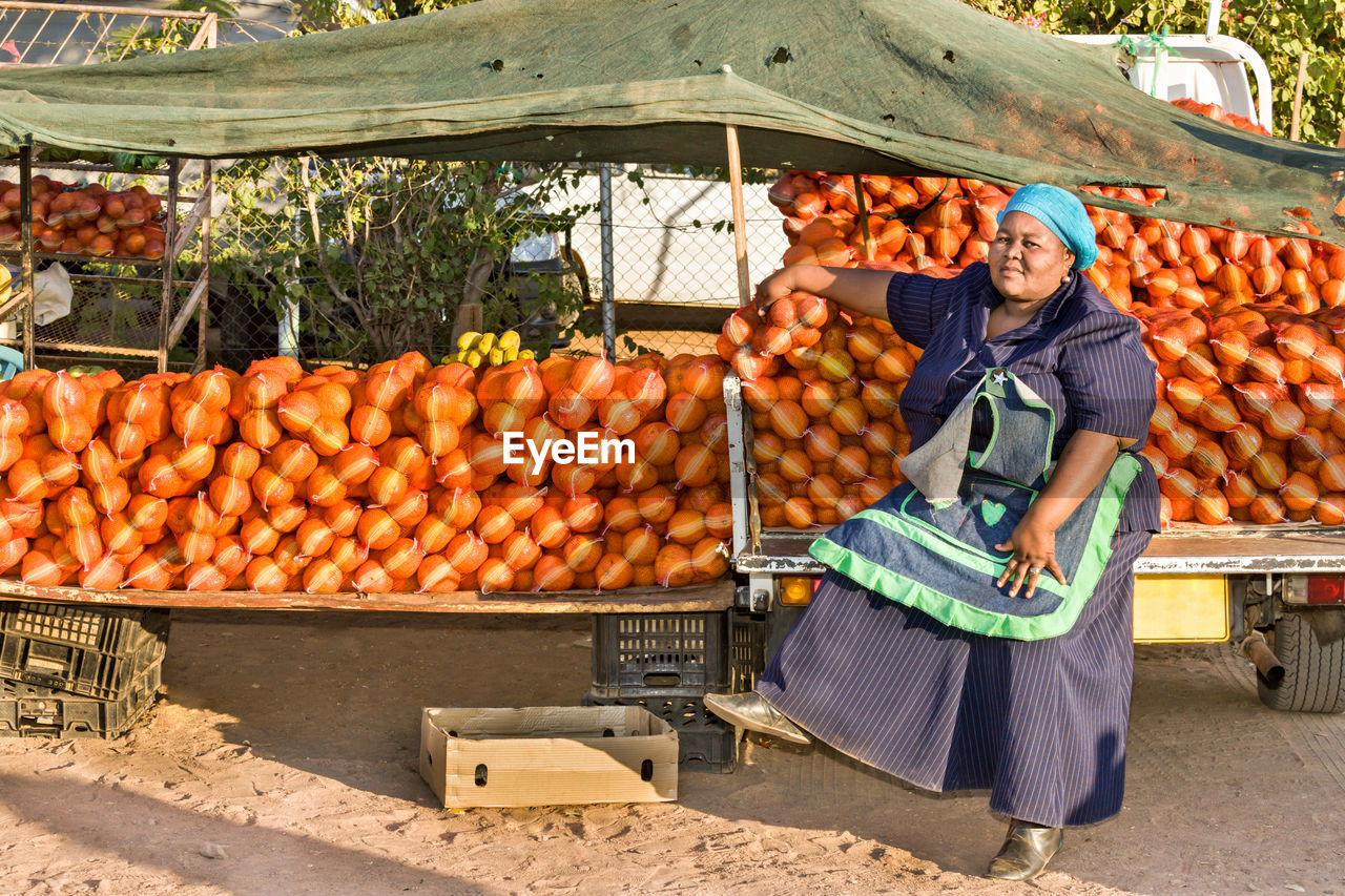 Full length of vendor sitting against food at market stall