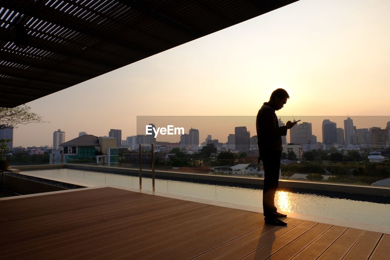 SILHOUETTE MAN STANDING BY BUILDING AGAINST SKY DURING SUNSET