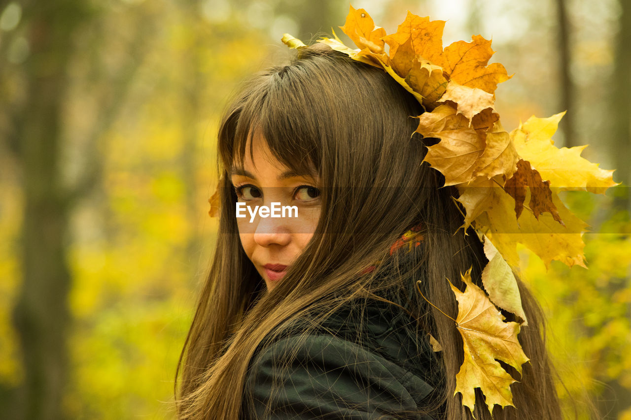 Portrait of smiling mid adult woman with autumn leaves on head at park