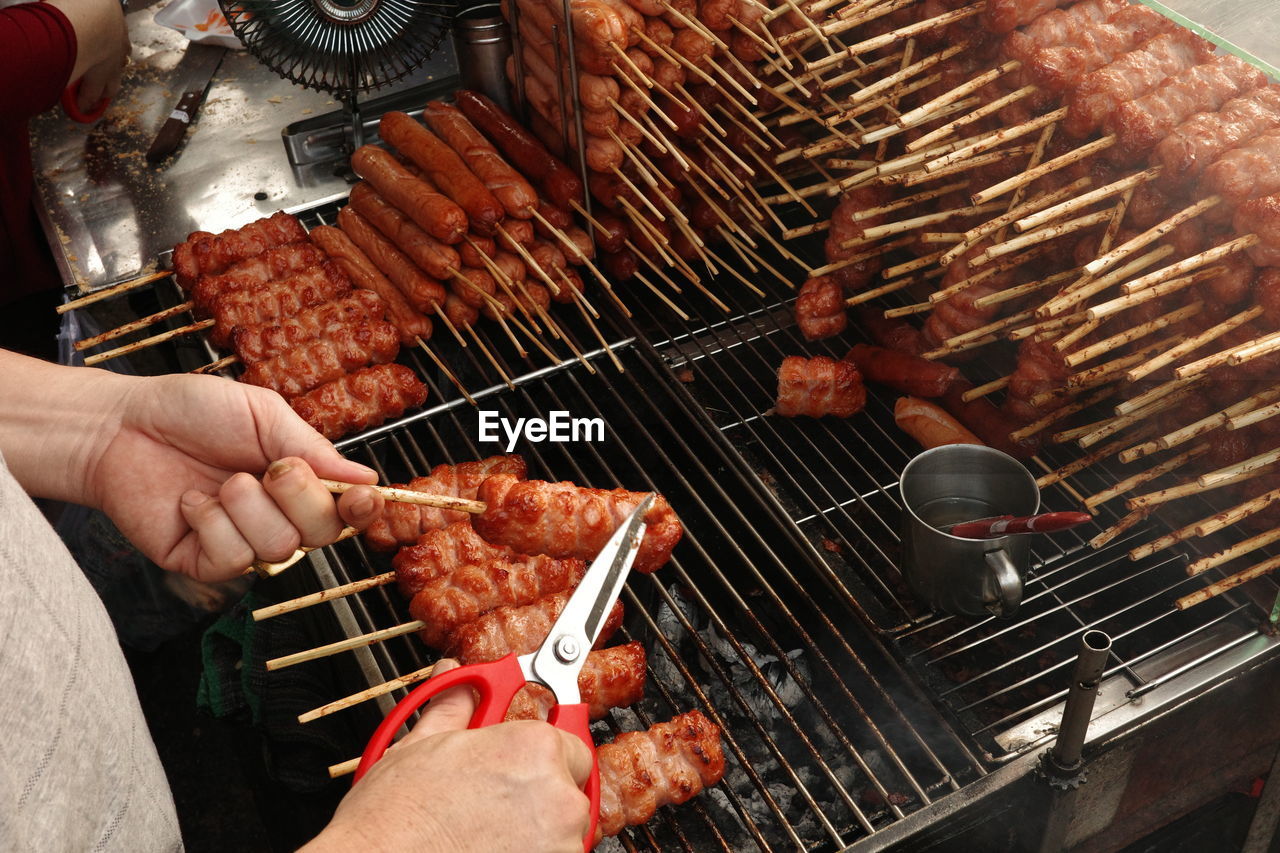 A close-up of a hand using a knife to cut a piece of grilled pork sausage. nem nuong ninh hoa.