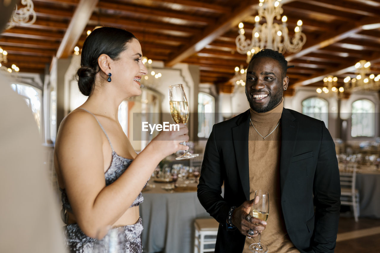 Beautiful young woman talking with male friends while drinking champagne at banquet