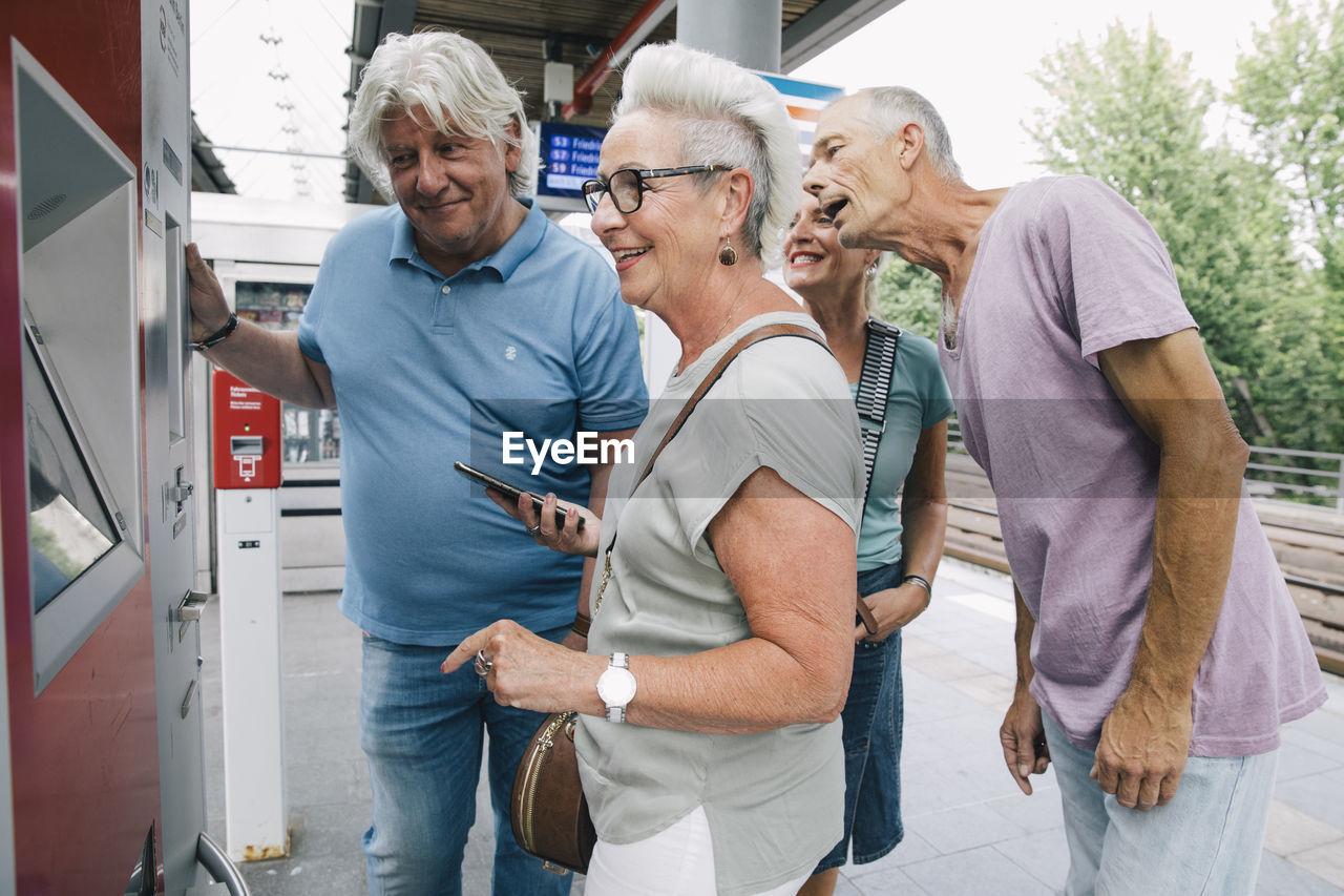 Group of senior friends buying ticket on railway station platform