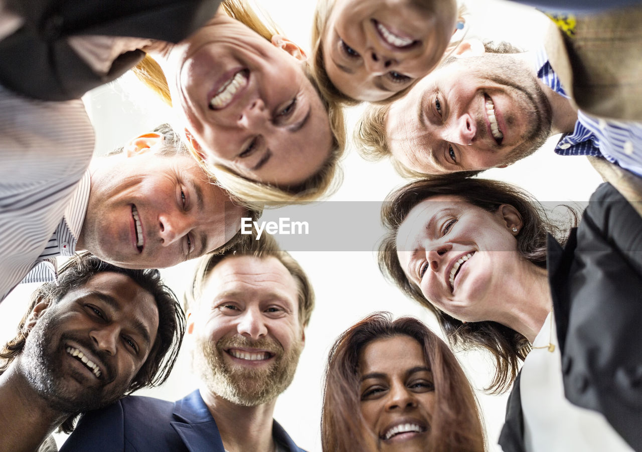 Directly below shot of business people forming huddle against clear sky