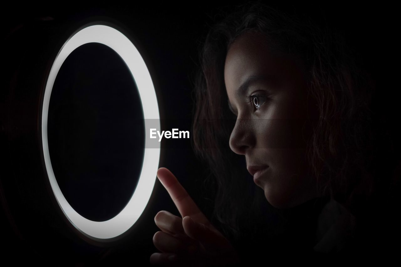 Close-up of girl looking at illuminated circle against black background