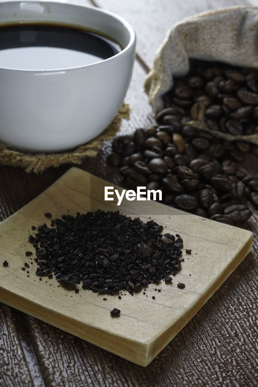 A cup of coffee, coffe beans and coffee powder on a wooden surface