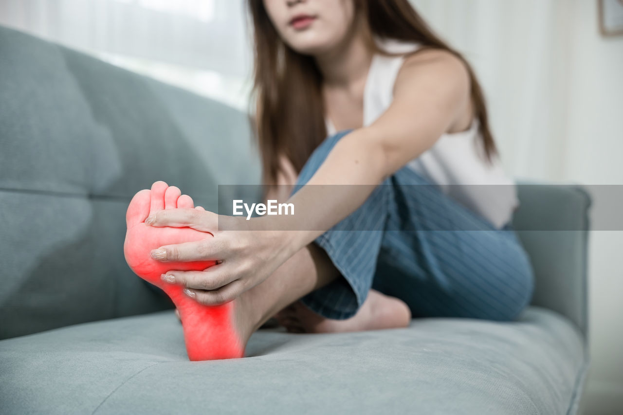 low section of woman sitting on bed at home