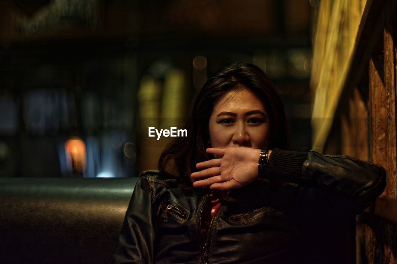 Portrait of woman covering mouth while standing by tree at night