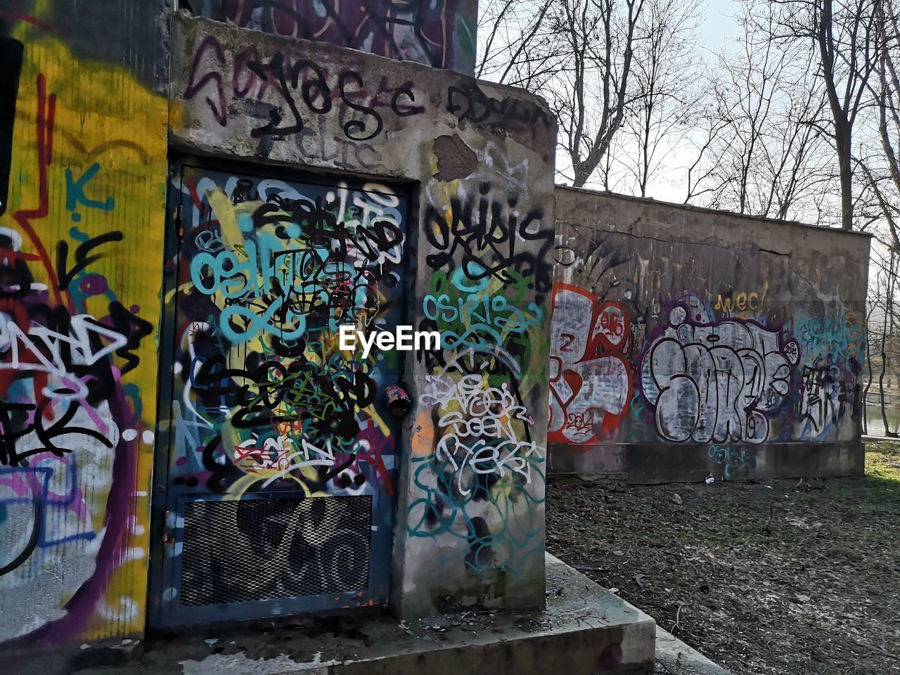 GRAFFITI ON WALL BY BARE TREES ON STREET