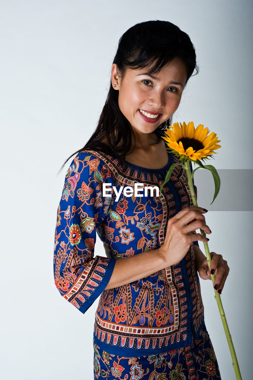 PORTRAIT OF SMILING YOUNG WOMAN HOLDING FLOWERS