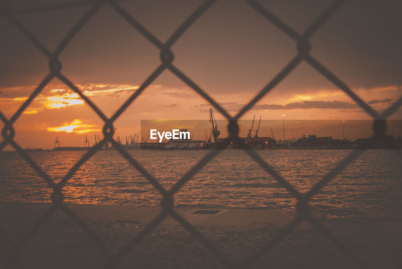Commercial dock by sea against sky seen from chainlink fence