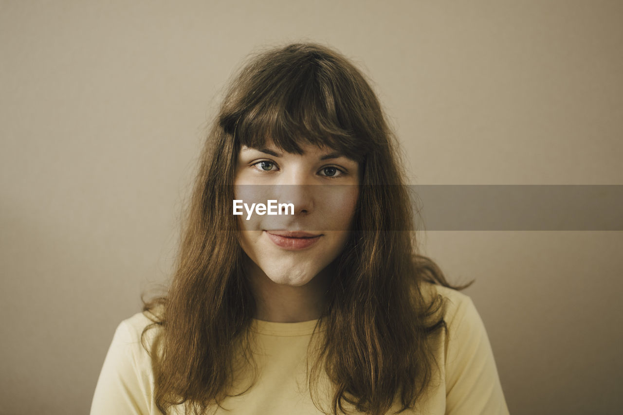 Portrait of young woman with bangs against beige background