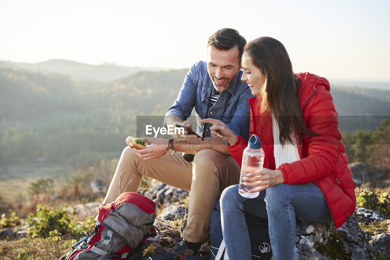 Happy couple on a hiking trip in the mountains taking a break looking at cell phone