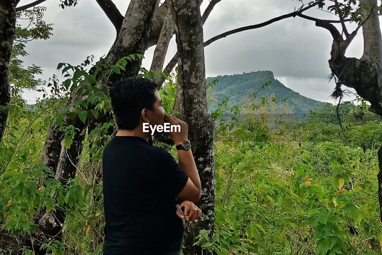 SIDE VIEW OF MAN STANDING BY TREE