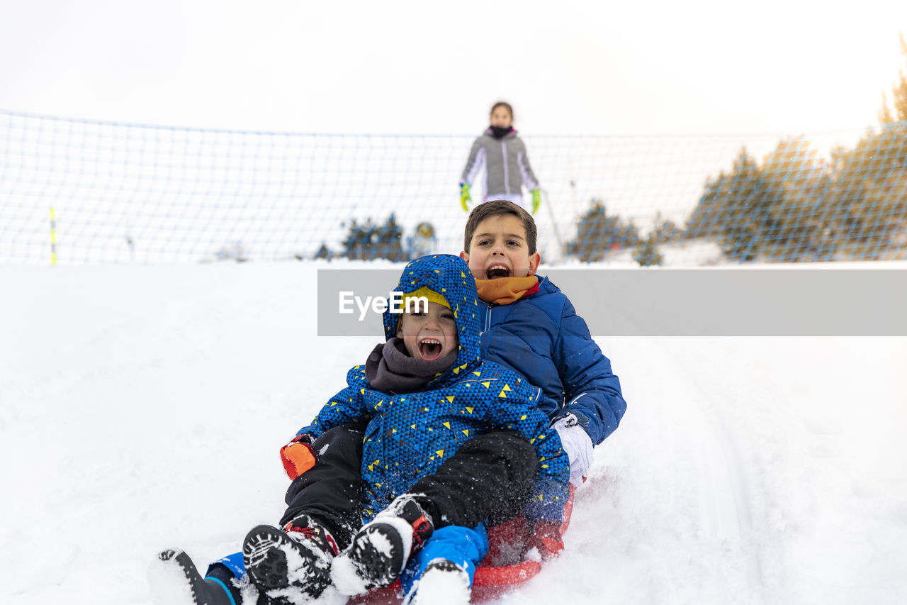 Full length of siblings tobogganing on snow during winter