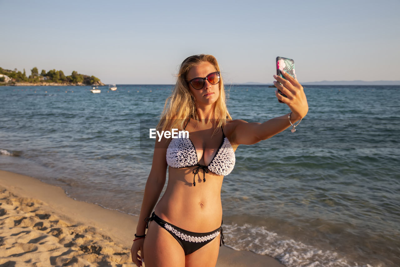 Portrait of a pretty attractive woman taking selfie. happy blonde girl next to the beach. aegean sea