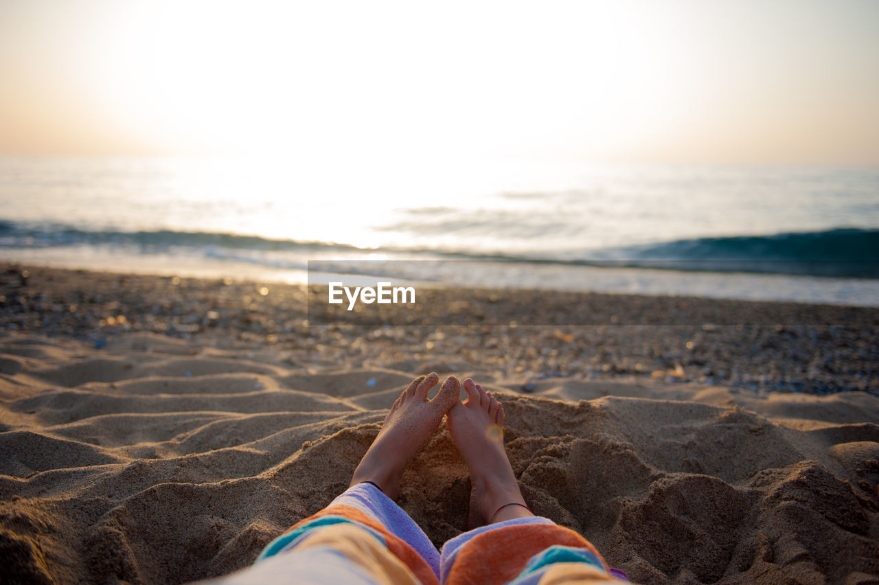 Low section of woman sitting on sand against sea at beach