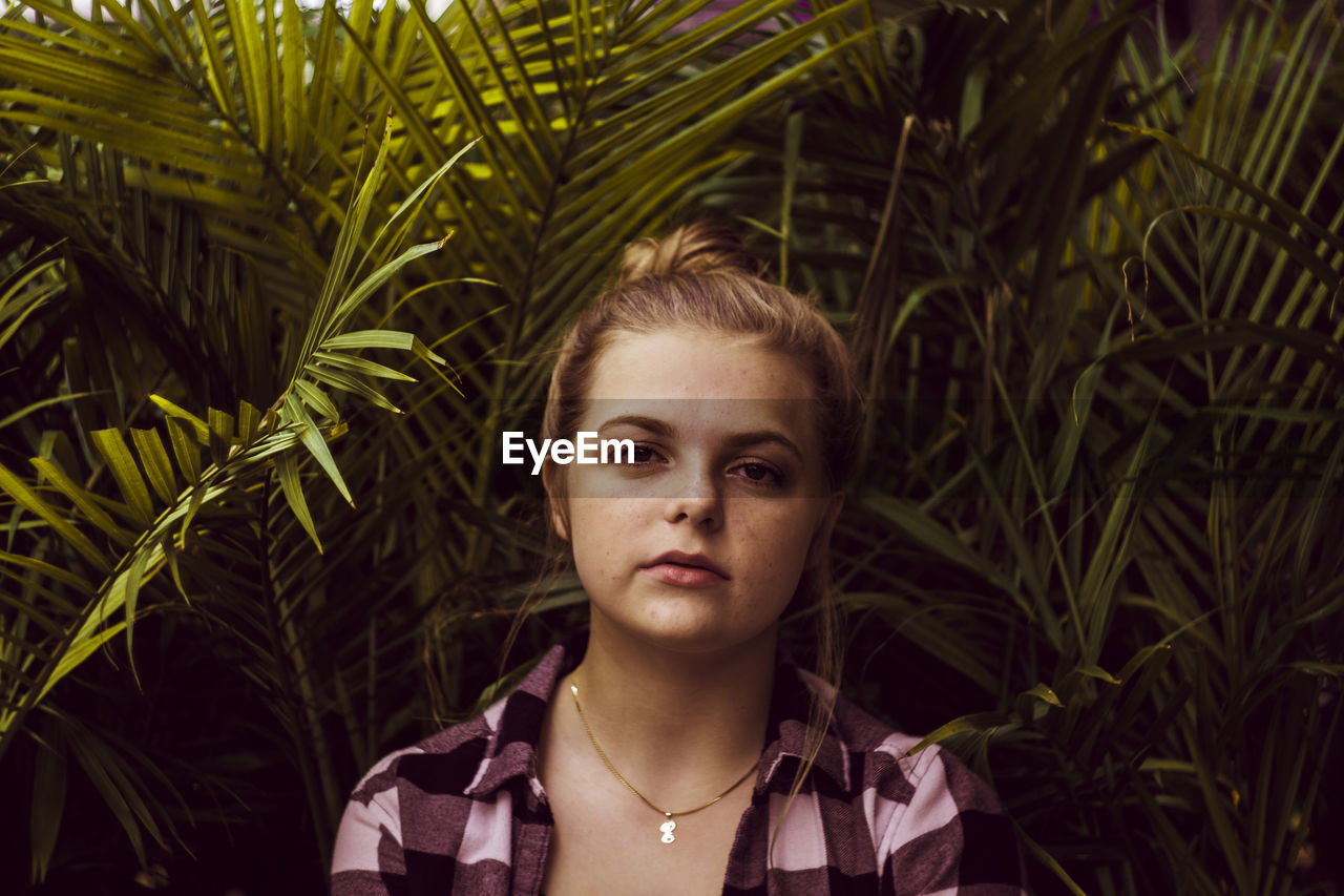 Close-up portrait of confident teenage girl against plants