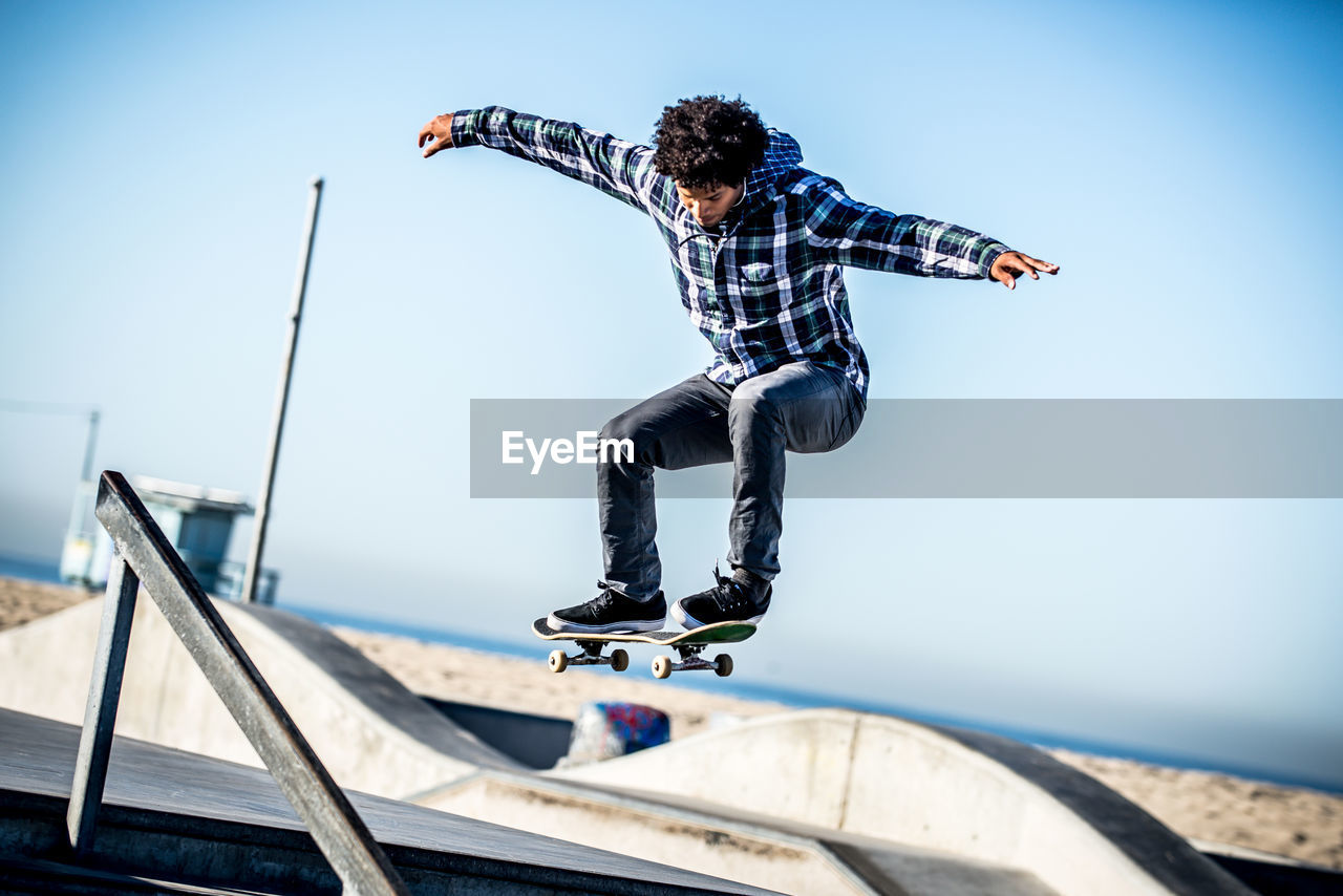 LOW ANGLE VIEW OF YOUNG MAN JUMPING AGAINST BLUE SKY