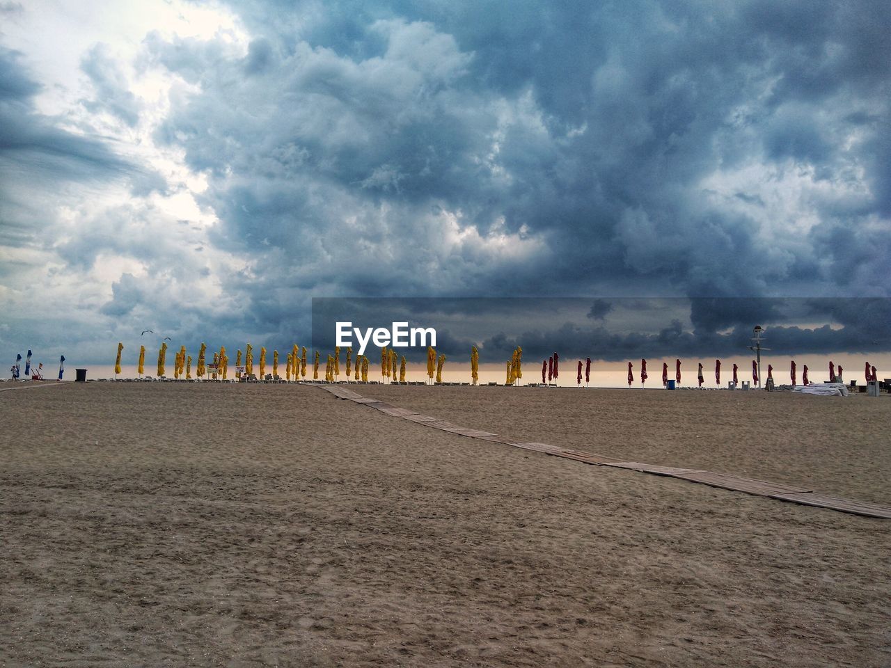 Distant view of closed parasols at beach against storm clouds