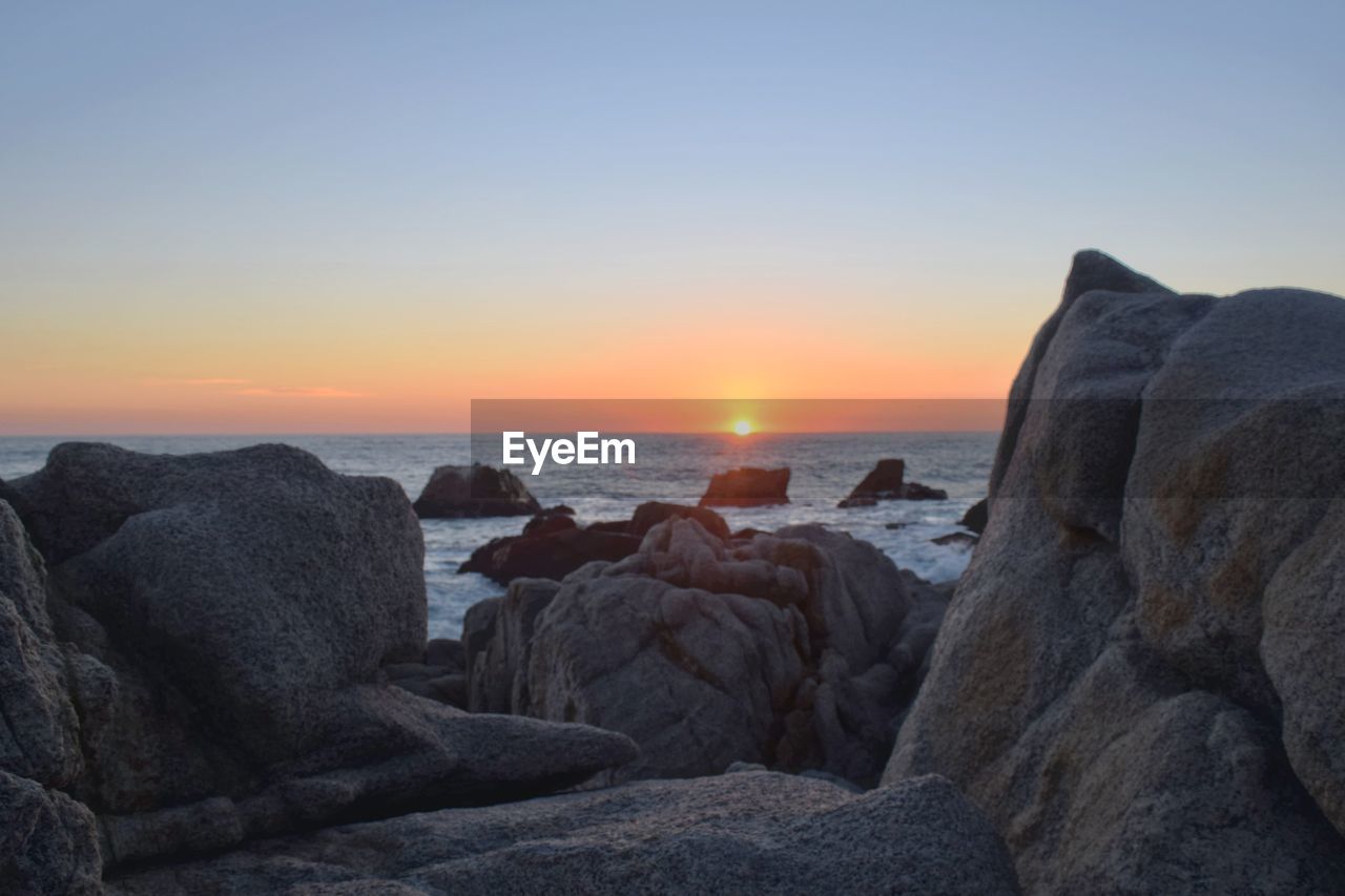 SCENIC VIEW OF ROCKS AT BEACH DURING SUNSET