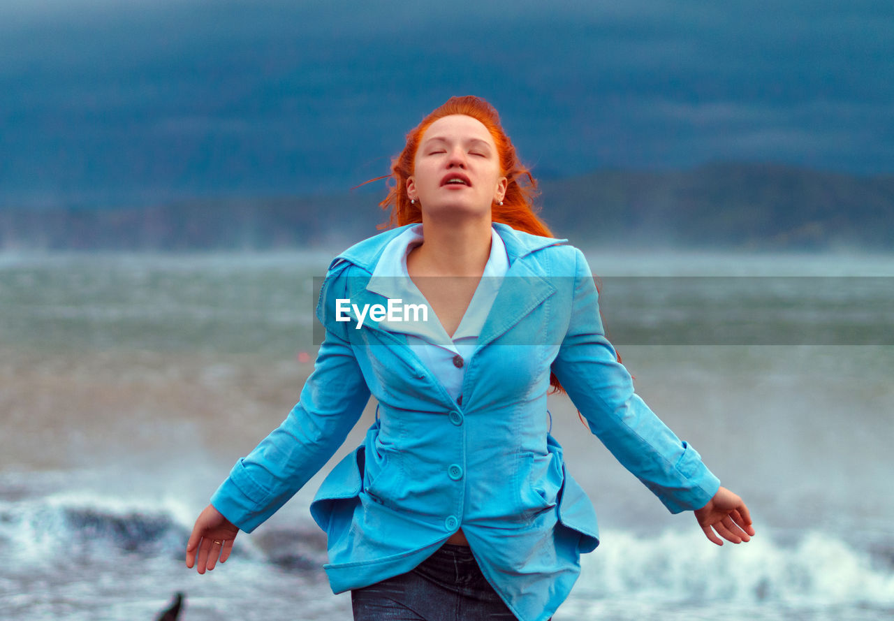 Carefree young woman with eyes closed standing at beach