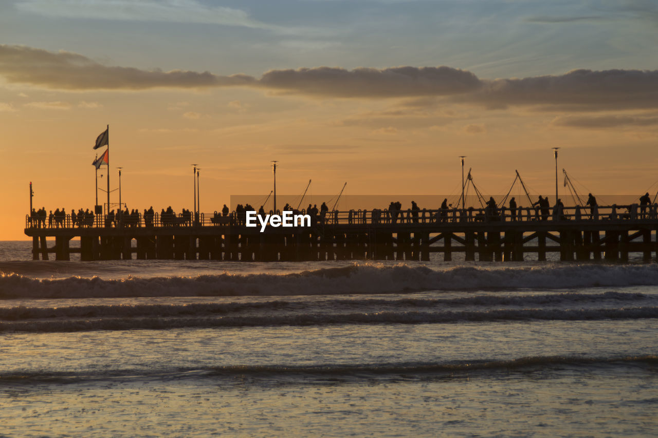 Silhouette people on pier over sea against sky during sunset