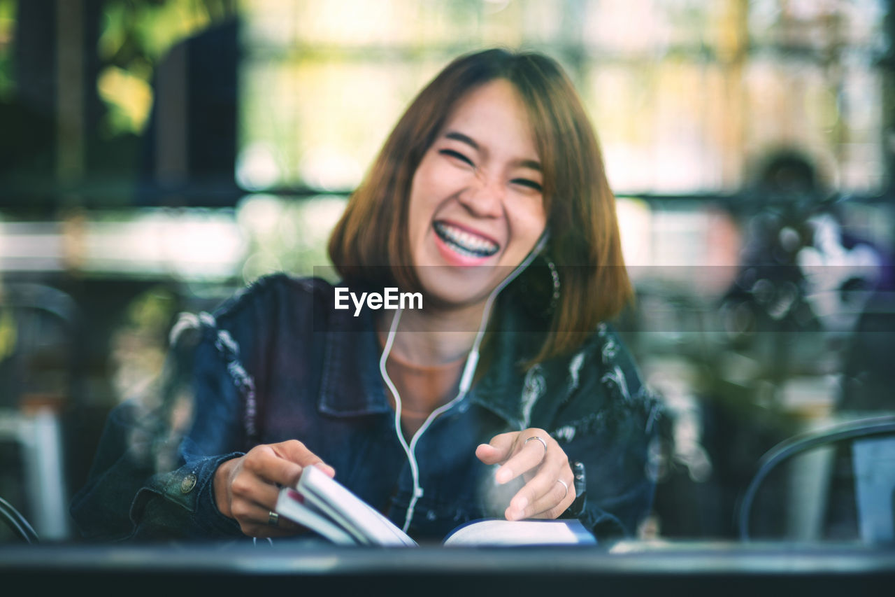 Portrait of cheerful young woman seen through glass sitting in cafe