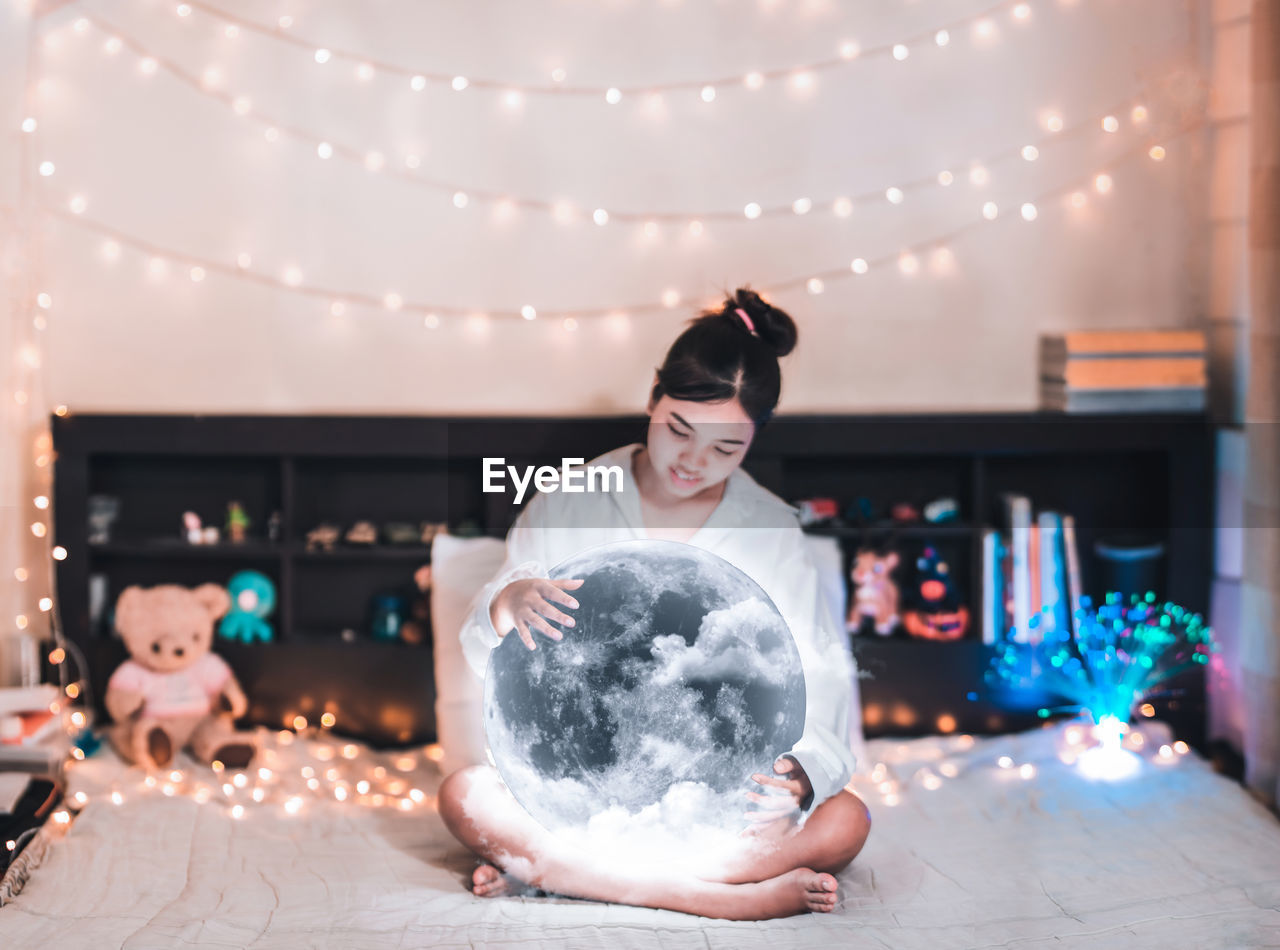 Digital composite image of young woman sitting with moon on bed