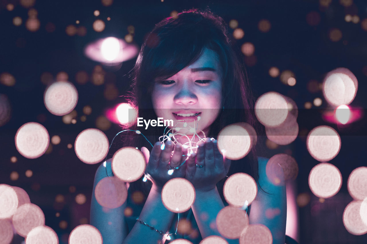 Close-up of smiling young woman holding illuminated lights at night