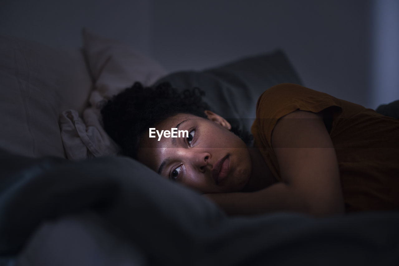 Pensive young woman lying in bed