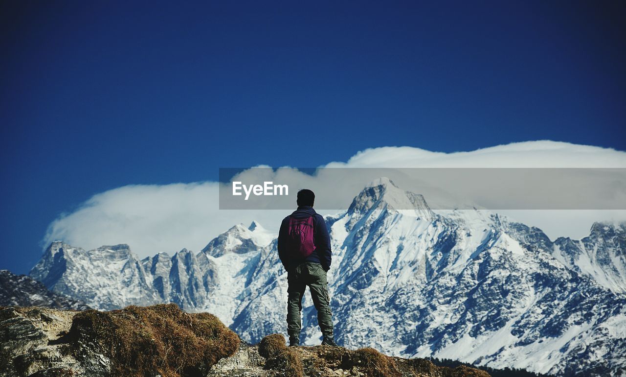 Rear view of man looking at snowcapped mountain against sky during winter