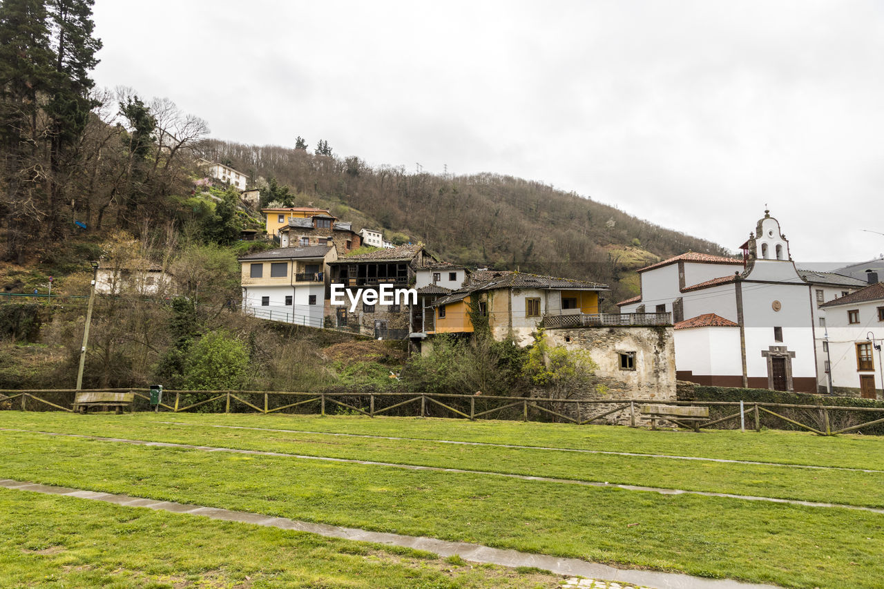 HOUSES ON GRASSY FIELD BY BUILDINGS AGAINST SKY