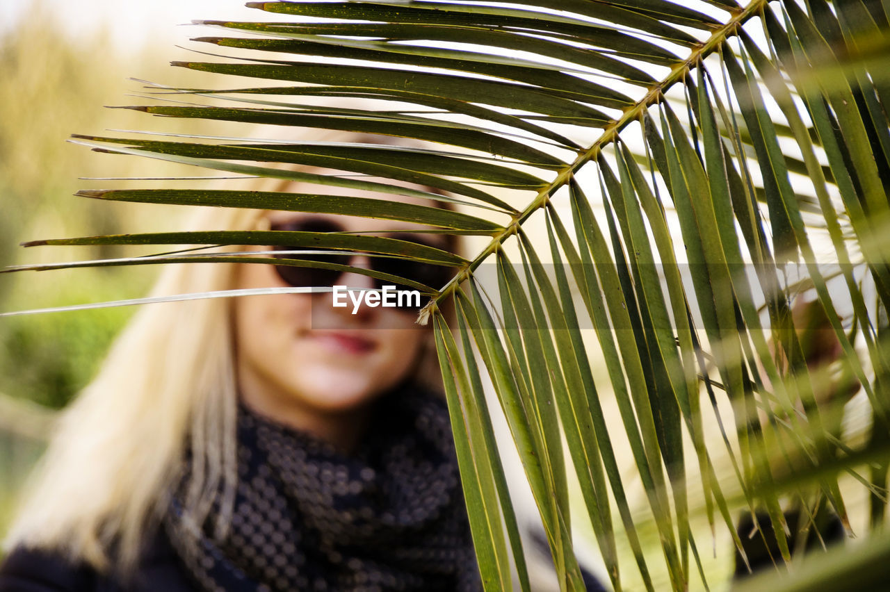 Portrait of young woman wearing sunglasses standing by leaf in park