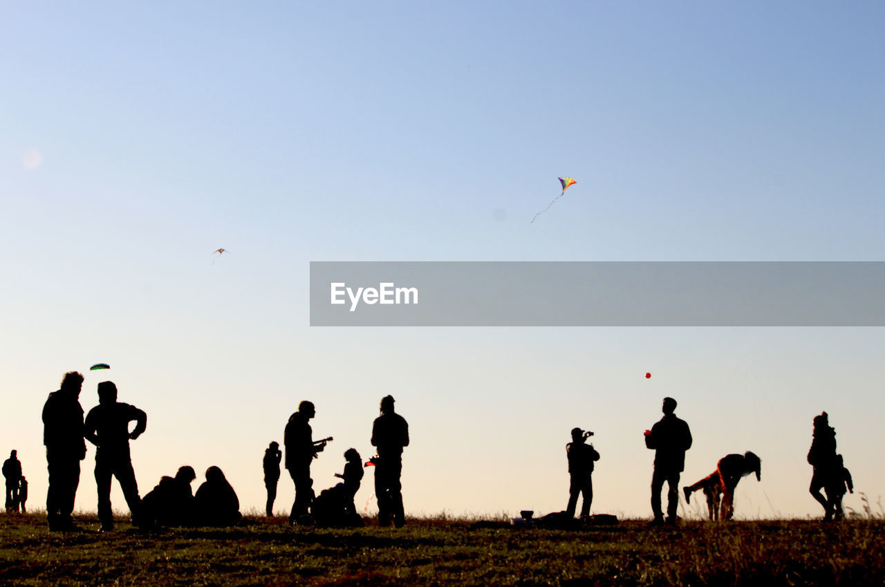 People flying kites on field against sky