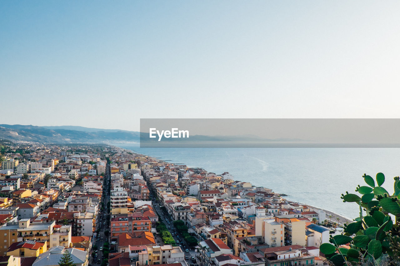 Aerial view of townscape by sea against clear sky