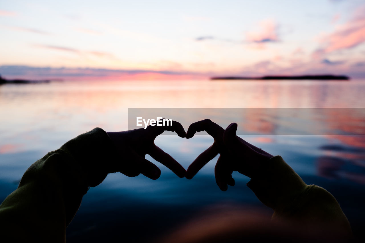 Heart shape hand gesture made with fingers against colorful out of focus sunset sky.  copy space.