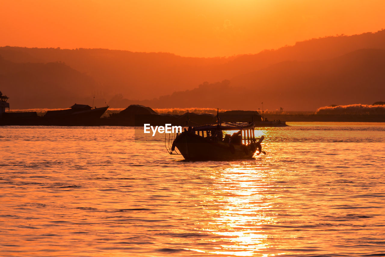 Silhouette boat in sea against orange sky