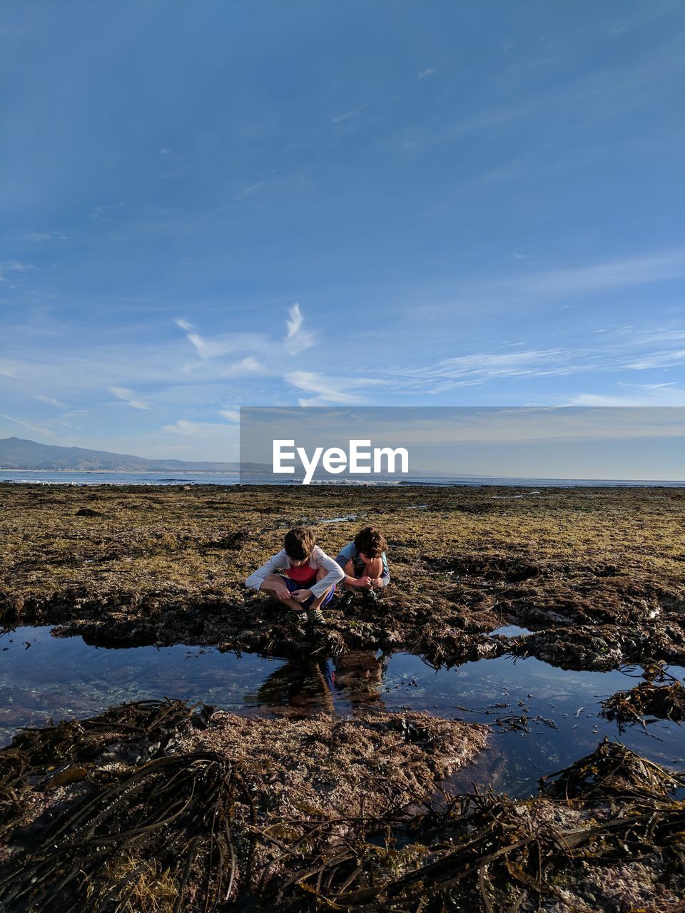 Friends crouching at beach against sky