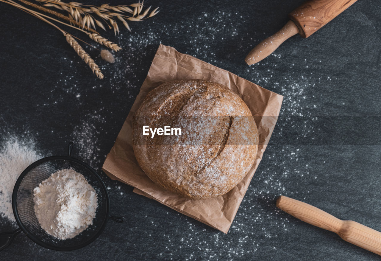 Round bread, sieve, rolling pins and ears on the table.