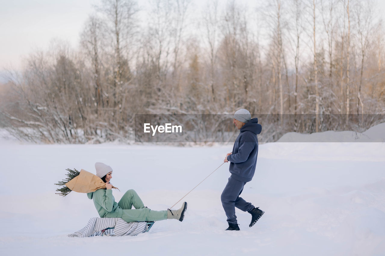 Smiling man giving sledding ride to woman. love and leisure concept.