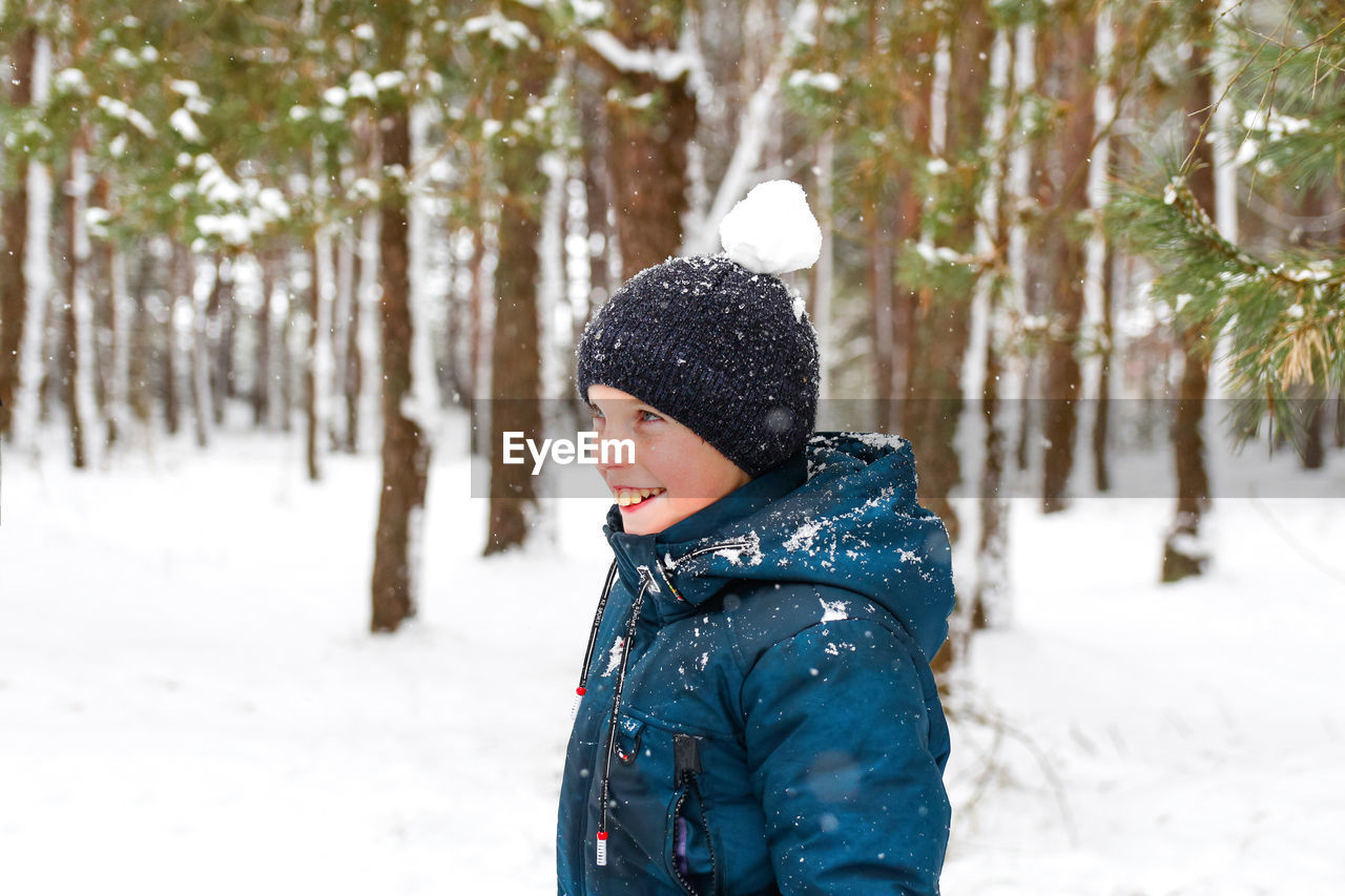 Smiling child boy in winter forest in snowstorm with snowball on head. funny kid on snowy winter 