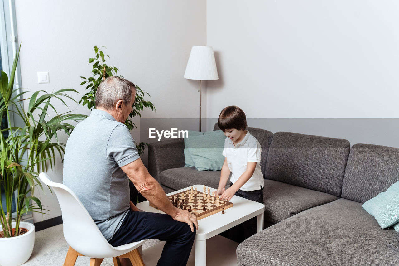 Little happy child and senior grandfather playing chess together at home. childhood hobby, education