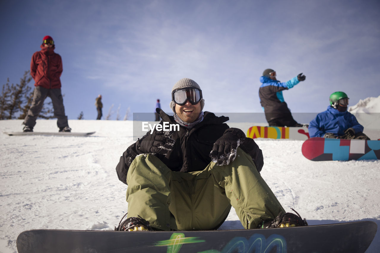 Cheerful friends with snowboarding on snowy field against sky