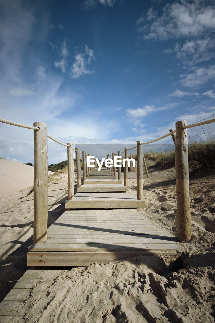 Wooden railing on beach against sky